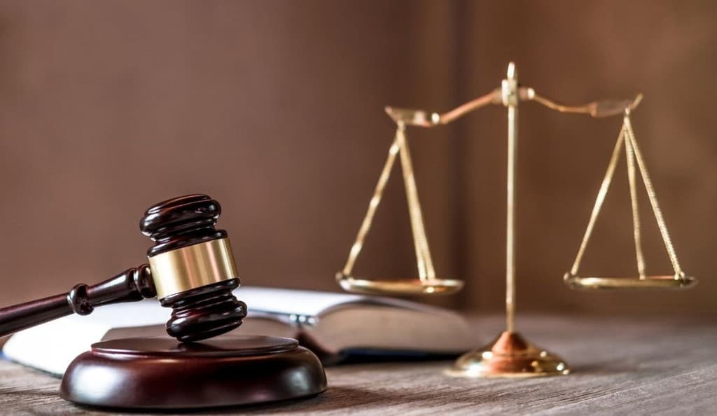 Wooden gavel with gold band and brass scales of justice on a desk